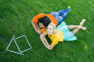 Couple lying on the grass with model house in front of them
